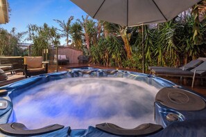 Un bain à remous entouré de chaises longues et de parasols, avec des plantes tropicales en arrière-plan.