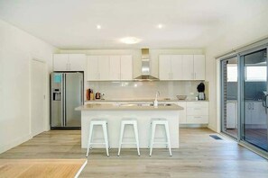 A modern kitchen with a central island, white cabinetry, a stainless steel refrigerator, and a glass door leading to a balcony.