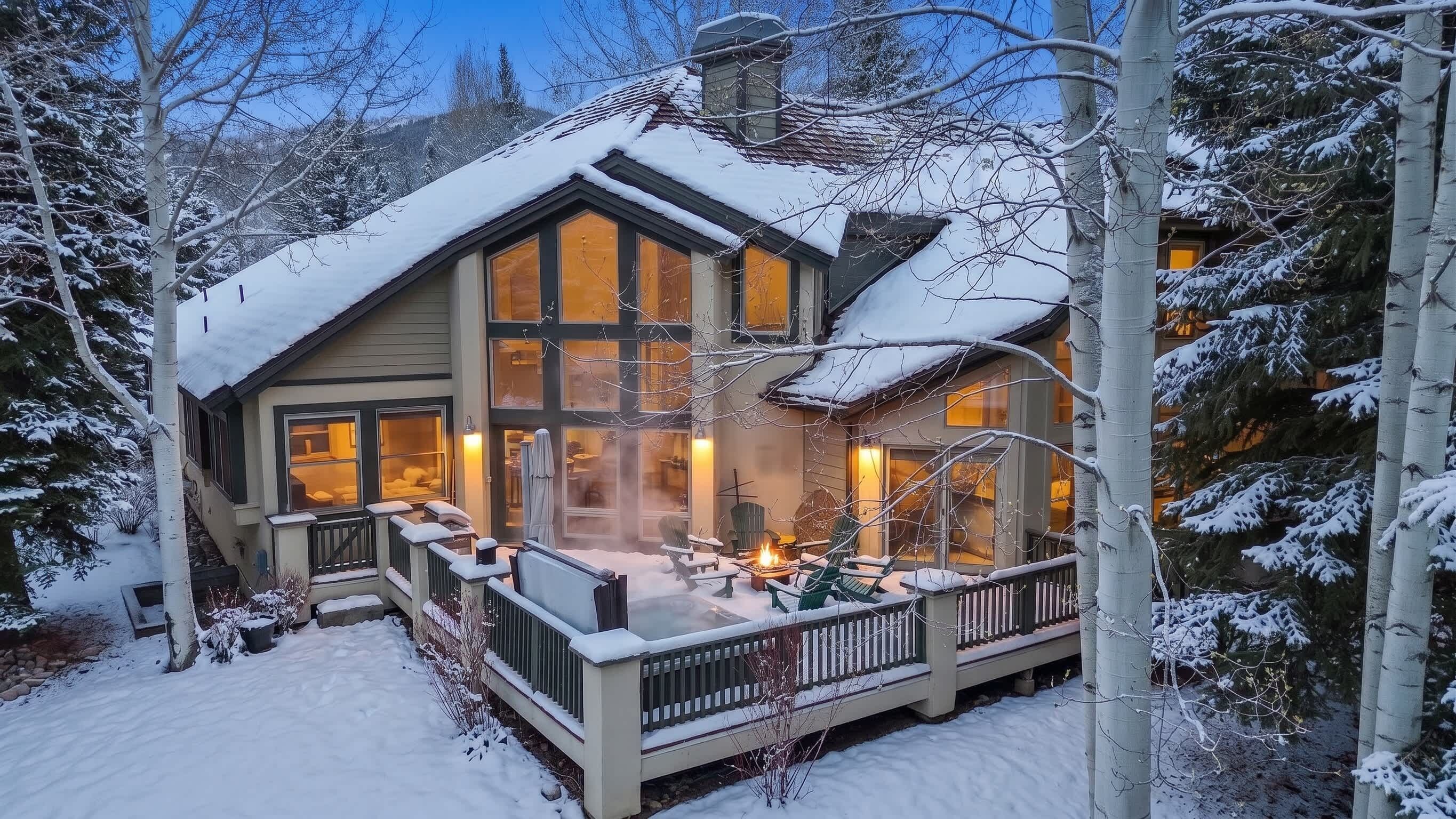 A two-story house with a deck, surrounded by snow-covered trees.
