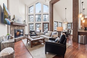 A spacious living room with a fireplace, large windows, a dining area, and a kitchen. - Castle Peak Close | Private Deck + Hot Tub + Grill (Edwards)