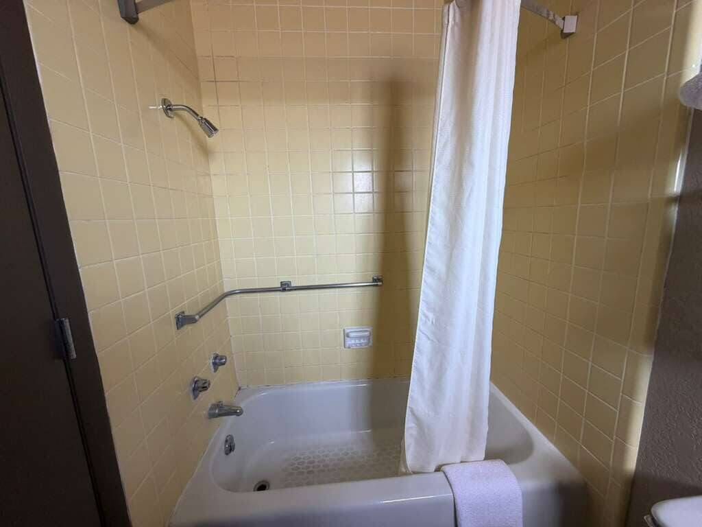 A bathroom with a bathtub, a shower curtain, and a handrail.