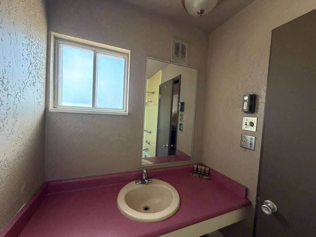 A bathroom with a sink, mirror, window, and a door.
