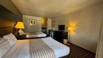 A hotel room with two beds, a desk, a chair, a television, and two lamps.