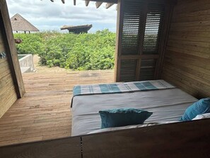 A wooden room with a bed, a window, and a view of greenery and a structure outside. - Punta Pájaros Villa 9 Puerto Escondido, Oaxaca (Puerto Escondido)
