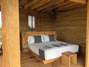 A wooden cabin bedroom with a bed, pillows, a bedside table, and a ceiling fan. - Punta Pájaros Villa 9 Puerto Escondido, Oaxaca (Puerto Escondido)
