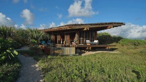 A modern, open-air structure with a large overhanging roof, a pool, and a pathway leading to the entrance.