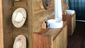 A wooden cabin bathroom with a wooden vanity, two sinks, a mirror, and three hats on the wall.