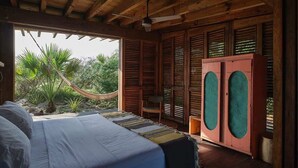 A bedroom with a bed, a hammock, wooden shutters, and a view of greenery.