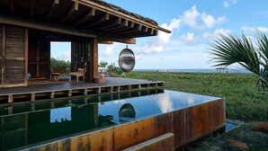 A wooden deck with a pool, a hanging chair, and a view of the ocean.