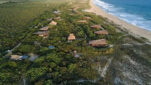 Eine Luftaufnahme eines Küstenresorts mit mehreren bungalowartigen Unterkünften, einem Strand und freiem Blick auf den Ozean.