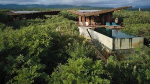 Eine rustikale Holzhütte mit Swimmingpool, umgeben von dichtem Grün und Bergen im Hintergrund.