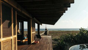 A wooden deck with a view of the ocean, a hanging chair, and a hot tub.