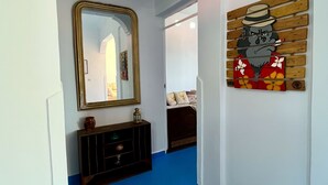 A hallway with a blue floor, a mirror, a wooden cabinet, and a wall-mounted artwork.