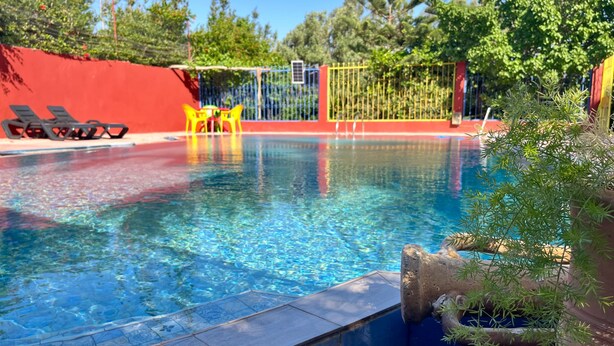 A swimming pool with clear water, surrounded by a red wall, a yellow fence, and a few lounge chairs.