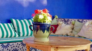 A blue wall, a striped sofa, a round wooden table, and a green and white vase with flowers.