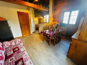 A cozy room with a wooden floor, a dining table with chairs, a bed with a patterned blanket, and a kitchen area with a stove and cabinets. - Chalet, terrace, balcony, tv, ski locker, 38m², Saint Gervais (Saint-Gervais-les-Bains)