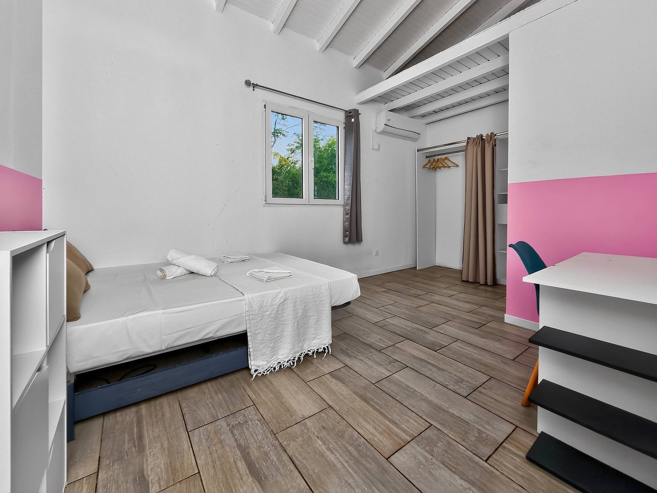 Un dormitorio con cama, escritorio, silla, ventana y armario.