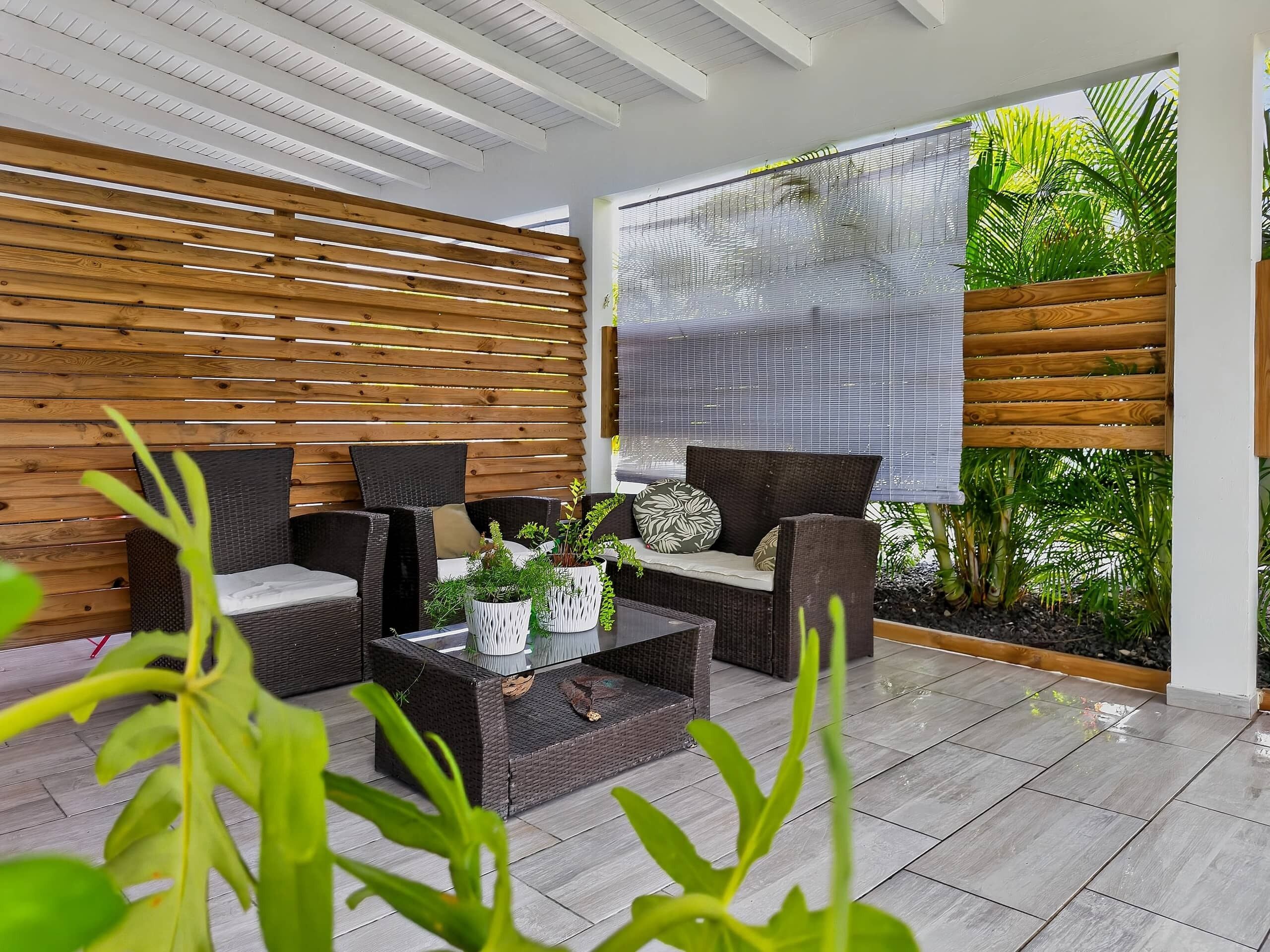 A modern outdoor seating area with wicker furniture, a glass coffee table, and a view of greenery through a window.
