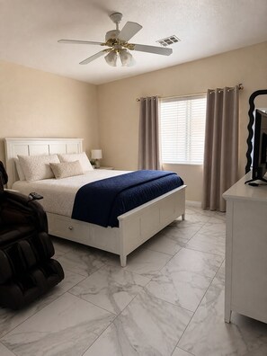 Ein Schlafzimmer mit einem Bett, einem Deckenventilator, einem Schreibtisch und einem Massagesessel.