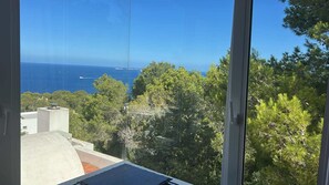 Blick durch ein Fenster auf einen klaren Himmel, Bäume und ein weiter Wasserblick.