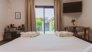 A hotel room with a bed, two towels, a desk with a coffee maker, a TV, and a view of greenery outside. - EDEN LUXURY ROOMS & GARDEN (Modugno)