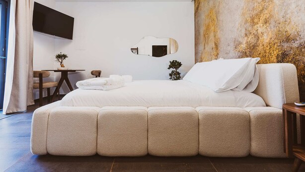 A modern bedroom with a large bed, a small table, a chair, a TV on the wall, and a unique textured wall. - EDEN LUXURY ROOMS & GARDEN (Modugno)