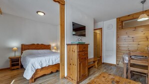 A wooden bed with a headboard, a wooden dresser, a wooden table, a bench, and a television mounted on the wall. - 40m from ski slopes, 1st floor, fitness, swimming pool, sauna, balcony, tv, ski locker, 34m² (Les Orres)