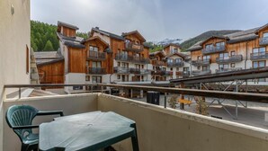 A balcony with a table and chairs, overlooking a row of wooden buildings with balconies. - 40m from ski slopes, 1st floor, fitness, swimming pool, sauna, balcony, tv, ski locker, 34m² (Les Orres)