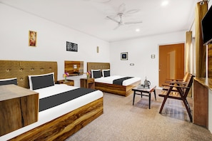 Habitación de hotel con tres camas, un escritorio, una silla, un televisor y un ventilador de techo.