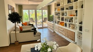 Una sala de estar moderna con un sofá, una mesa de centro con flores, una estantería y vistas a través de un ventanal.