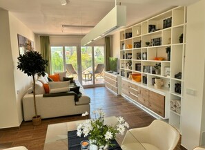 A modern living room with a sofa, a coffee table with flowers, a bookshelf, and a view through a glass door. - Luxurious apartment garden pool beach 300 meters view of Africa Gibraltar (La Línea de la Concepción)