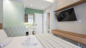 Ein Hotelzimmer mit Bett, Fernseher, Badezimmer mit Spiegel und grüner Wand.