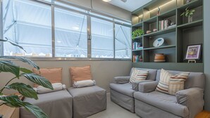 Ein modernes Wohnzimmer mit zwei grauen Sofas, einem Holztischchen, einem großen Fenster mit Blick und einem grünen Bücherregal.