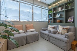 Ein modernes Wohnzimmer mit zwei grauen Sofas, einem Holztischchen, einem großen Fenster mit Blick und einem grünen Bücherregal.