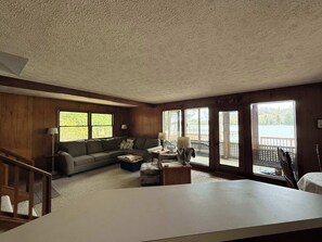 Ein Zimmer mit Holzboden, einer Couch, einem Couchtisch, einer Lampe und großen Fenstern mit Seeblick.