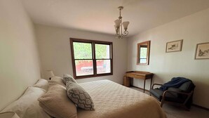 Een slaapkamer met een bed, een bureau, een stoel, een raam en een kroonluchter.