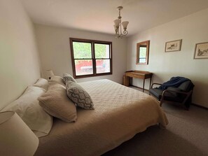 Ein Schlafzimmer mit Bett, Schreibtisch, Stuhl, Fenster und einer Chandelier.