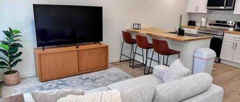 Eine moderne Küche mit Mikrowelle, Backofen und Spüle. Ein Holzschrank beherbergt einen Flachbildfernseher, und es gibt eine Sitzecke mit Sofa und Sesseln.