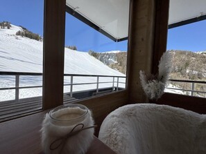 Ein Zimmer mit Blick auf eine verschneite Landschaft, ein weißes, flauschiges Objekt und eine Kerze auf einem Tisch.