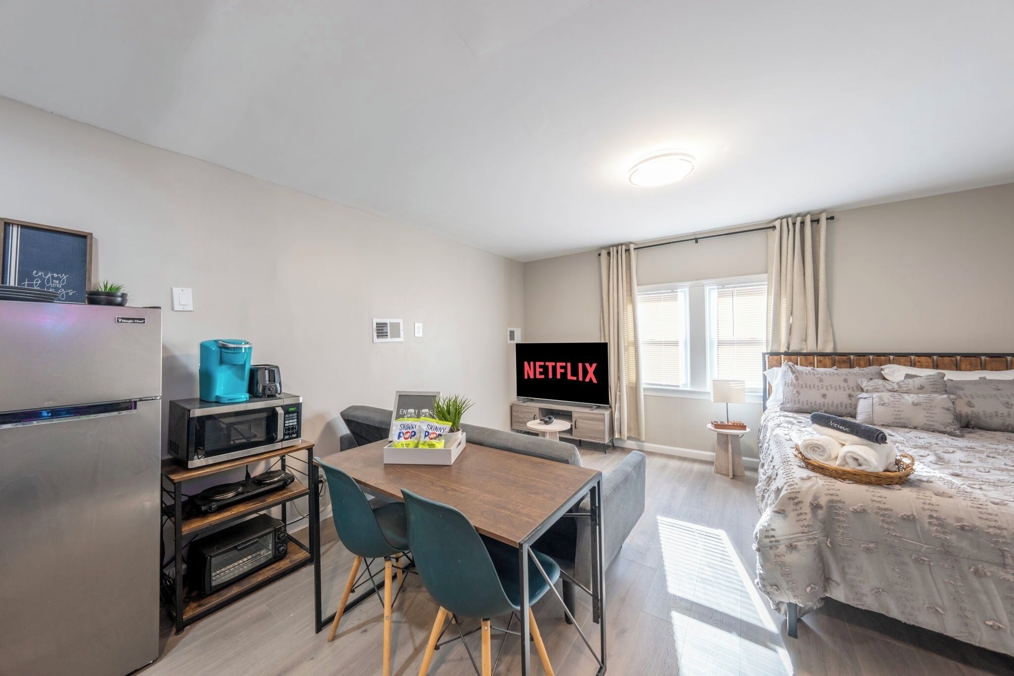 A compact hotel room with a kitchenette, a dining area, a bed, and a TV displaying 'NETFLIX'.