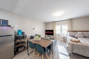 Camera d'albergo compatta con angolo cottura, zona pranzo, un letto e una TV che mostra 'NETFLIX'.