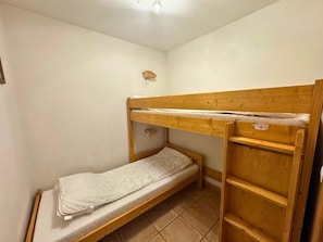 Ein kleines Zimmer mit einem Einzelbett, einem Stockbett, einer kleinen Ablage und einem fest montierten Heizkörper.