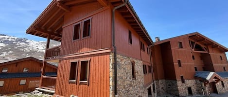 Ein mehrstöckiges Holzgebäude mit Balkonen, darunter eine Steinfassade, und ein freier Blick auf die Berge im Hintergrund.