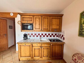 A compact kitchen with wooden cabinets, a microwave, a stove, and a checkered backsplash. - Ground floor, balcony, tv, ski locker, 35m², Les Menuires (Les Menuires)