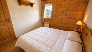 Ein Zimmer mit Holzwänden, einem Bett, einem Fenster mit Vorhängen und einem an der Wand befestigten Regal.