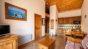 Ein Wohnzimmer mit Holz-TV-Schrank, einer Couch, einem Holztisch und einer Küchenzeile mit Holzschränken und einer Fliesenrückwand.