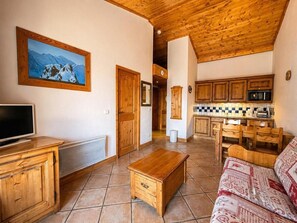 A living room with a wooden TV stand, a sofa, a wooden coffee table, and a kitchen area with wooden cabinets and a tiled backsplash. - 2nd floor, balcony, tv, ski locker, 32m², Les Menuires (Les Menuires)