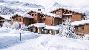 Ein Chalet-Hotel im Holzbau mit mehreren Gebäuden, verschneiten Dächern und einer Bergkulisse.