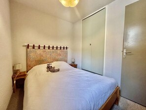 Ein Schlafzimmer mit einem Bett, einem Nachttisch, einer Lampe, einem Kleiderschrank und einer Tür.