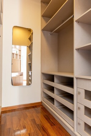 A walk-in closet with open shelving and drawers, wooden flooring, and a mirror on the wall. - Casa com 4 Quartos - Alto Padrão (Carapicuíba)